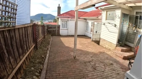 Paved side yard sloped to drain, with a gravel strip along the fence line