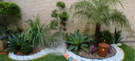 Desert-style planting bed with a white river rock border, palm, agaves and a pot along a wall