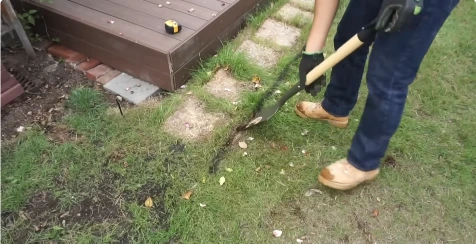 Landscaper string-trimming weeds and grass around stepping stones near a deck
