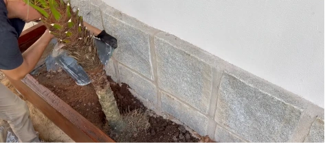 Landscaper removing old soil from a timber-edged bed along a wall