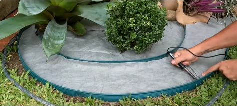 Landscape fabric weed barrier being cut and laid around a shrub in a circular bed